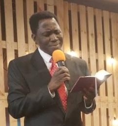 Pastor Bethuel Matsili trzymający mikrofon i Biblię podczas nabożeństwa.